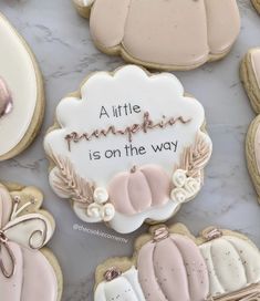 cookies decorated with pink and white frosting on a marble counter top that says a little pumpkin is on the way