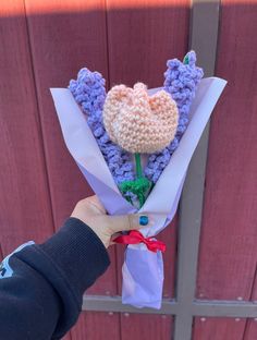 someone is holding a crocheted flower bouquet in front of a wooden door with a red ribbon