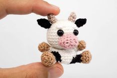 a small crocheted cow is being held up by someone's hand,