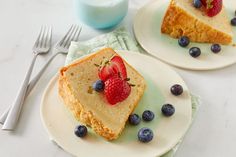 two slices of cake on plates with blueberries and strawberries in the middle, next to a glass of milk