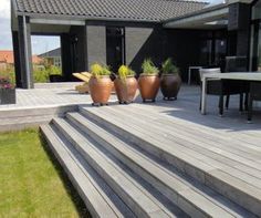 some plants are sitting in large pots on the steps outside an open house with patio furniture