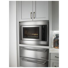 an oven built into the wall in a kitchen with white cabinets and stainless steel appliances