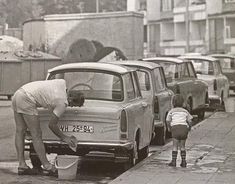 an old black and white photo of two women washing cars in the street with children nearby