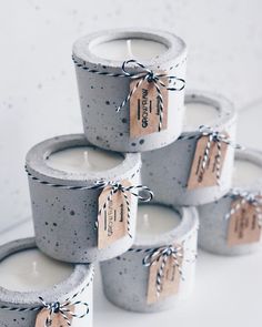 four candles with tags on them sitting next to each other in cement pots and tied with twine