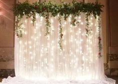 the wedding backdrop is decorated with flowers and greenery, along with white sheer curtains