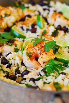 a pan filled with rice, shrimp and black beans next to lime wedges on the side