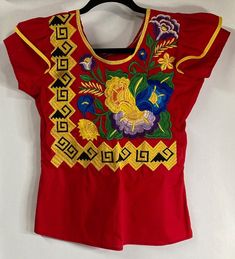 Oaxaca Embroidered Blouse with Floral and Earth Serpent Design in Red Size XS/SM   #118-G Oaxaca traditional blouse with embroidered floral design and Zapotec symbol. Called the earth serpent, this symbol represents a temple and a mountain, both which were sacred to the Zapotecs.  Red with yellow accents- it has a round neckline and ruffles at the sleeves.  This traditional styled blouse is made by hand/sewing machine.  It does not have a brand tag, size tag, or care tag.  It is 100% cotton, but without elasticity.  Garment runs small, especially in the bust.  Please review measurements.   Wash by hand recommended. All measurements are approximate, and have been taken from a flat garment: 16" Underarm to underarm 15" Near waist 22" Shoulder to end of shirt Red Embroidered Top For Festive Occasions, Red Fitted Embroidered Top For Festivals, Red Festive Tops For Festivals, Fitted Red Embroidered Top For Festivals, Red Embroidered Blouse For Festivals, Red Blouse With Embroidered Border For Festivals, Red Embroidered Tops For Festivals, Festive Red Short Sleeve Tops, Red Folk Tops With Floral Embroidery