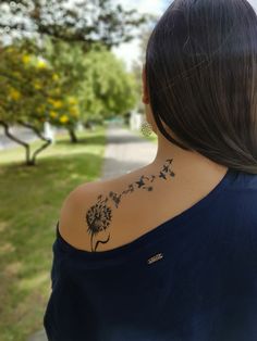 the back of a woman's shoulder with a dandelion tattoo on it