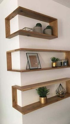 three wooden shelves on the wall with plants and pictures in them, one is empty