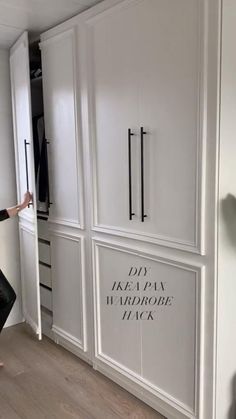 a woman standing in front of a white closet with black lettering on the doors and drawers