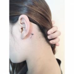 a woman's left ear has a tiny cross tattoo on it