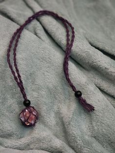 a necklace with a pink bead hanging from it's end on a gray blanket