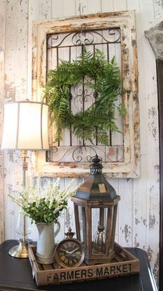 a table topped with a lamp next to a wall mounted clock and a green wreath