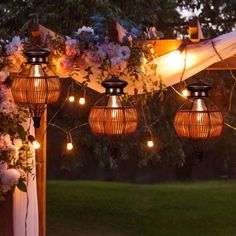 some lights hanging from a wooden structure with flowers and greenery on the outside wall