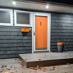 an orange door sits in front of a black house with autumn leaves on the ground