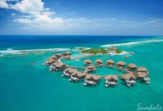 an aerial view of a resort in the middle of the ocean with thatched roofs