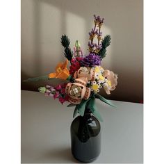 a vase filled with lots of colorful flowers on top of a white table next to a wall