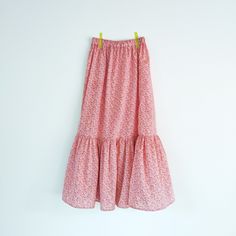 a pink floral dress hanging on a white wall with yellow clothes pins attached to it