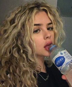 a close up of a person drinking from a water bottle with long curly blonde hair