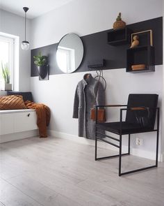 a room with a chair, mirror and coat rack on the wall next to a window