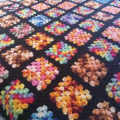 a multicolored crocheted blanket is laying on the floor next to a bed