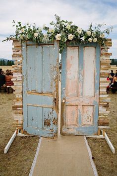 an old blue door with flowers on it and some people sitting in the back ground