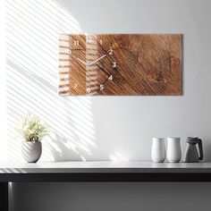 a wooden clock mounted to the side of a wall next to two mugs and a plant