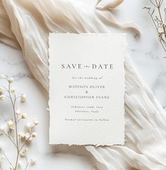 a white wedding save the date card on top of a table next to some flowers