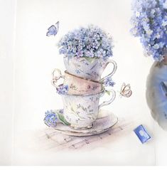 two cups with flowers in them sitting next to a vase filled with purple and blue flowers