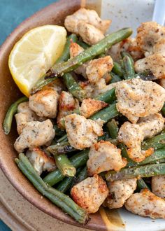 a bowl filled with chicken and green beans next to a slice of lemon wedged in the side