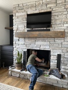 a man sitting in front of a fireplace with a tv above it and plants on the mantle