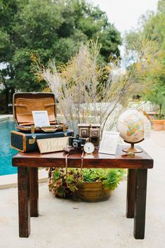 an open suitcase sitting on top of a wooden table next to a pool and trees