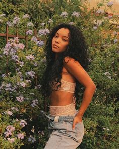 a young woman standing in front of some flowers wearing ripped jeans and a bra top