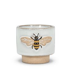 a white and yellow vase with a bee painted on it's side, in front of a white background