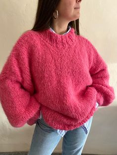 a woman standing in front of a wall wearing a pink sweater