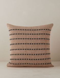 a black and tan pillow on a white table with a beige wall in the background