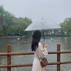 a woman holding an umbrella while standing next to a lake