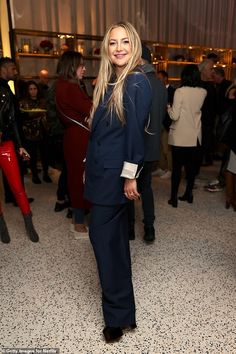 a woman standing in front of a crowd wearing a blue suit and white shirt with black shoes