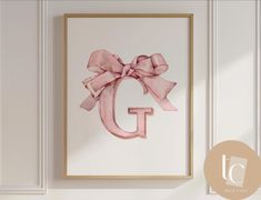 a pink bow hangs on the wall above a framed letter g with a gold frame