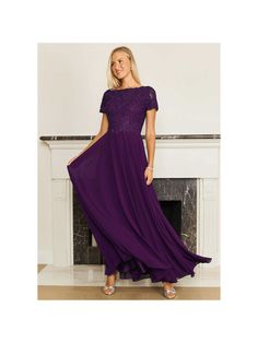 a woman wearing a purple dress standing in front of a fireplace with her hands on her hips