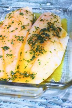 two fish fillets in a glass dish with herbs on the top and seasonings on the bottom