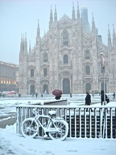 a bicycle is parked in front of a building with snow on the ground and people walking around