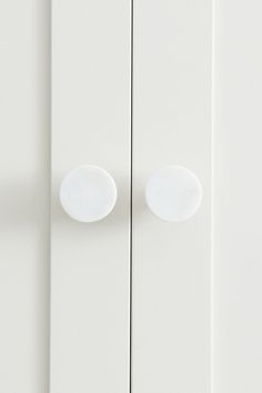 a white cabinet with two round knobs on the front and back doors, against a white wall