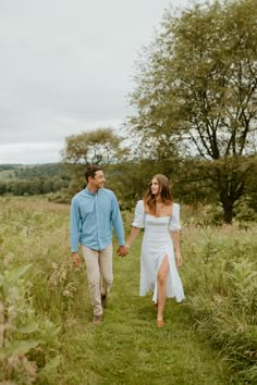 a man and woman holding hands while walking through tall grass in the middle of a field