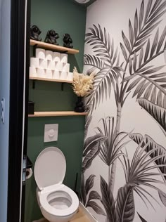 a toilet in a bathroom with palm trees on the wall and shelves above it,