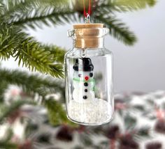 a snowman ornament in a glass jar hanging from a christmas tree branch