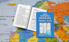 the sudoku puzzles travel size book is open on a world map and it's contents are laid out