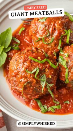 a white plate topped with meatballs covered in sauce and garnished with basil