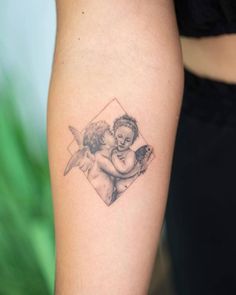 an angel tattoo on the arm of a woman's left arm, with a small cherub holding a baby