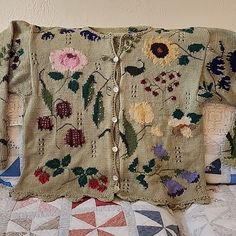 an old sweater with flowers on it is sitting on a quilted tablecloth covered bed